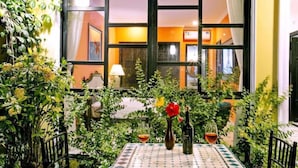 A table with a vase and wine glasses, surrounded by greenery, in front of a window with a view of an interior space. - Sunshine Villa Hoi An (Da Nang)