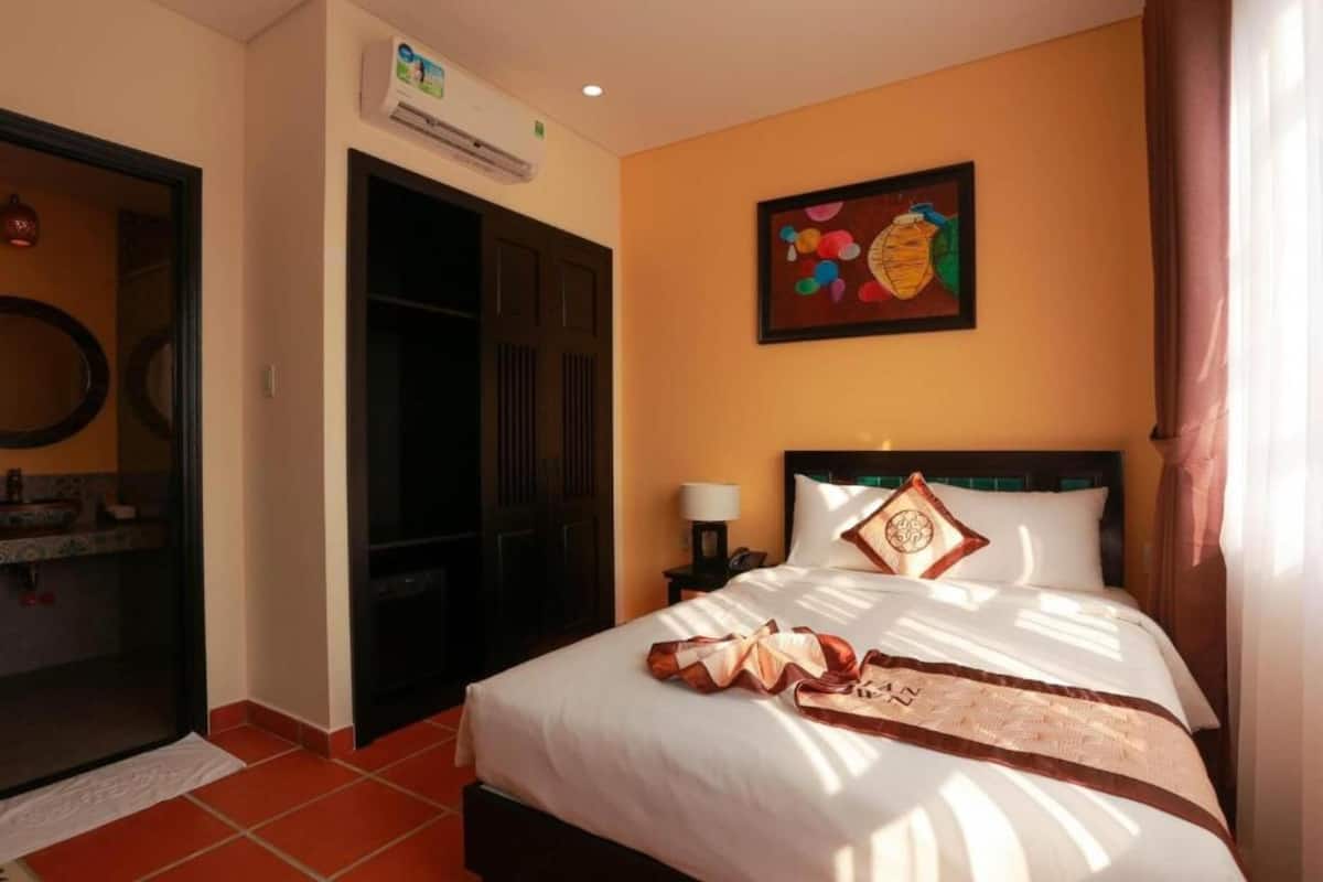 A hotel room with a bed, a nightstand, a wall-mounted air conditioner, and a painting.