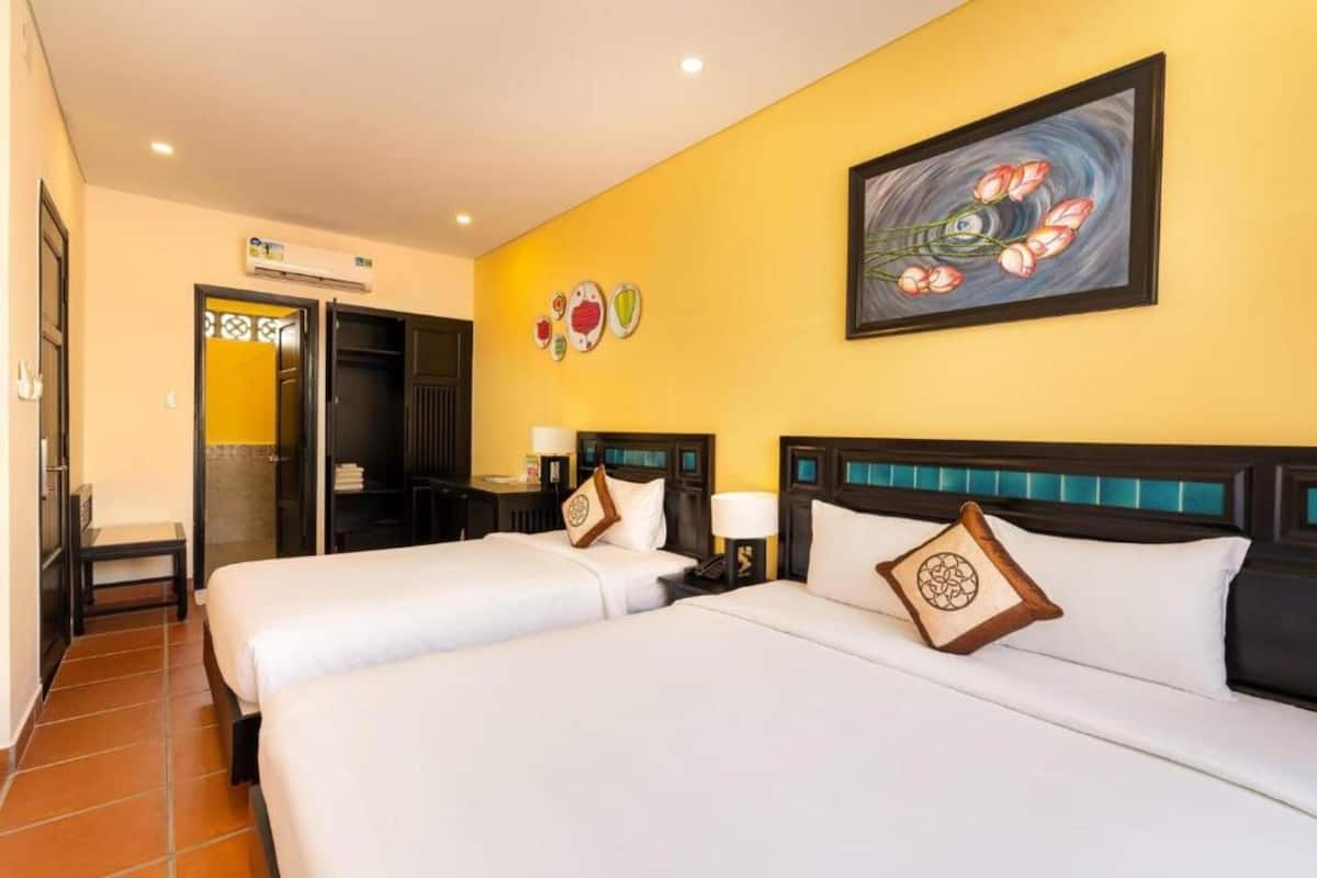 A hotel room with two beds, a painting, and a wall with decorative plates.