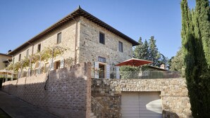 A stone building with a garage, a staircase, and a small balcony with a red umbrella. - The Casaloni app. Tower (Panzano In Chianti)