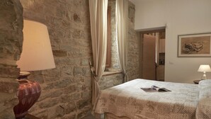 A bedroom with stone walls, a bed with a quilt, a lamp, and a window with curtains. - The Casaloni app. Tower (Panzano In Chianti)