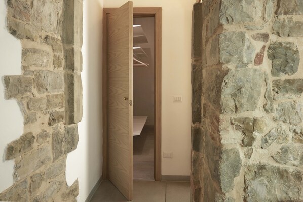 A narrow hallway with stone walls and a wooden door leading to a room with a built-in closet and a staircase. - Casaloni Tour Apartment (Panzano In Chianti)