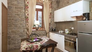 A kitchen with stone walls, a dining table with floral tablecloth, and modern appliances. - The Casaloni app. Tower (Panzano In Chianti)