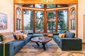 A cozy living room with a large window, a wooden ceiling, and a dog painting on the wall.