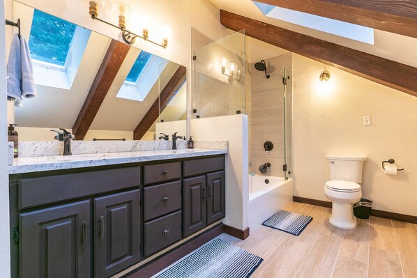 Un baño moderno con tragaluz, ducha a ras de suelo y un espejo grande.