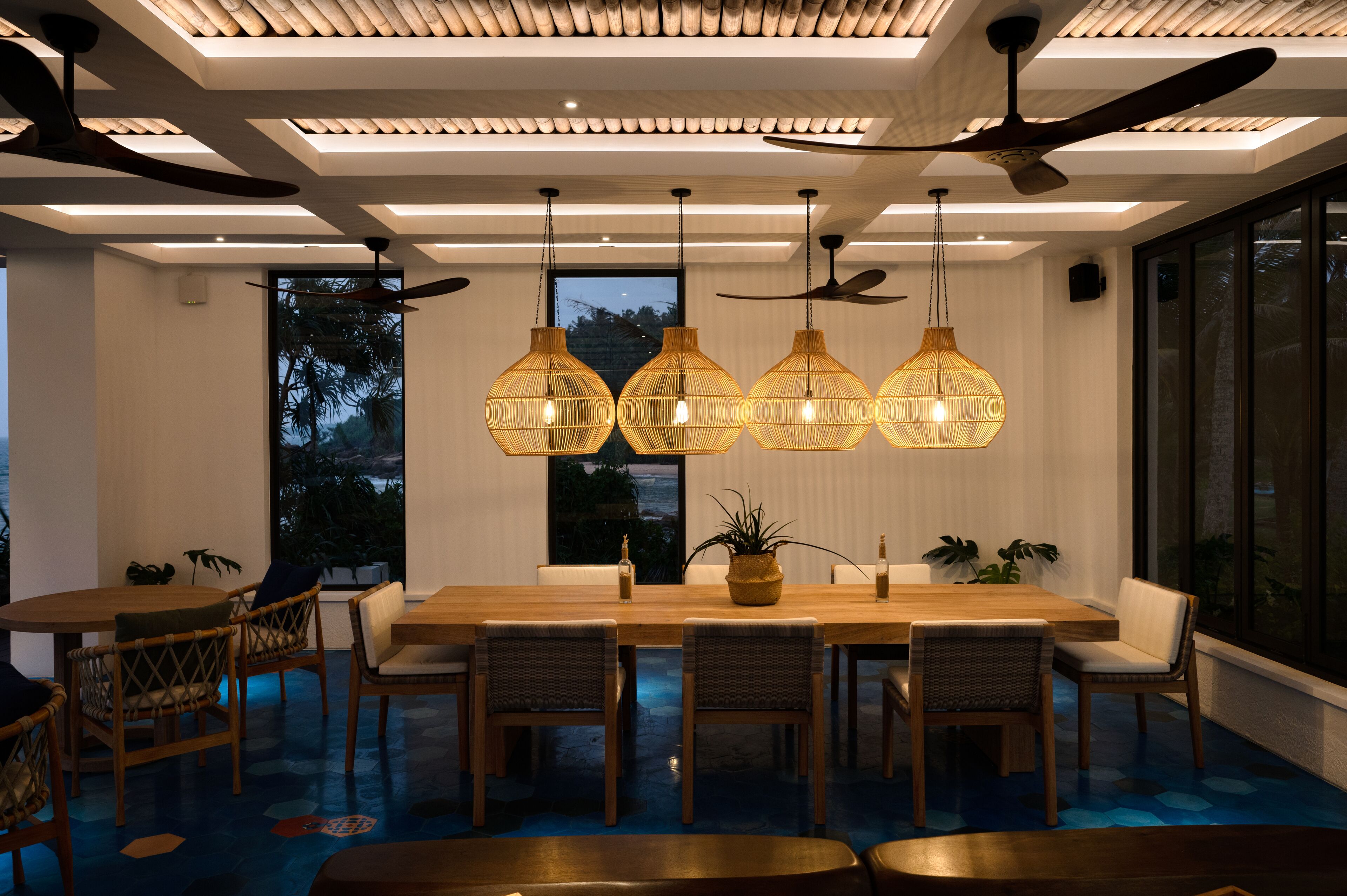 A modern dining area with a long wooden table, wicker chairs, and pendant lights.