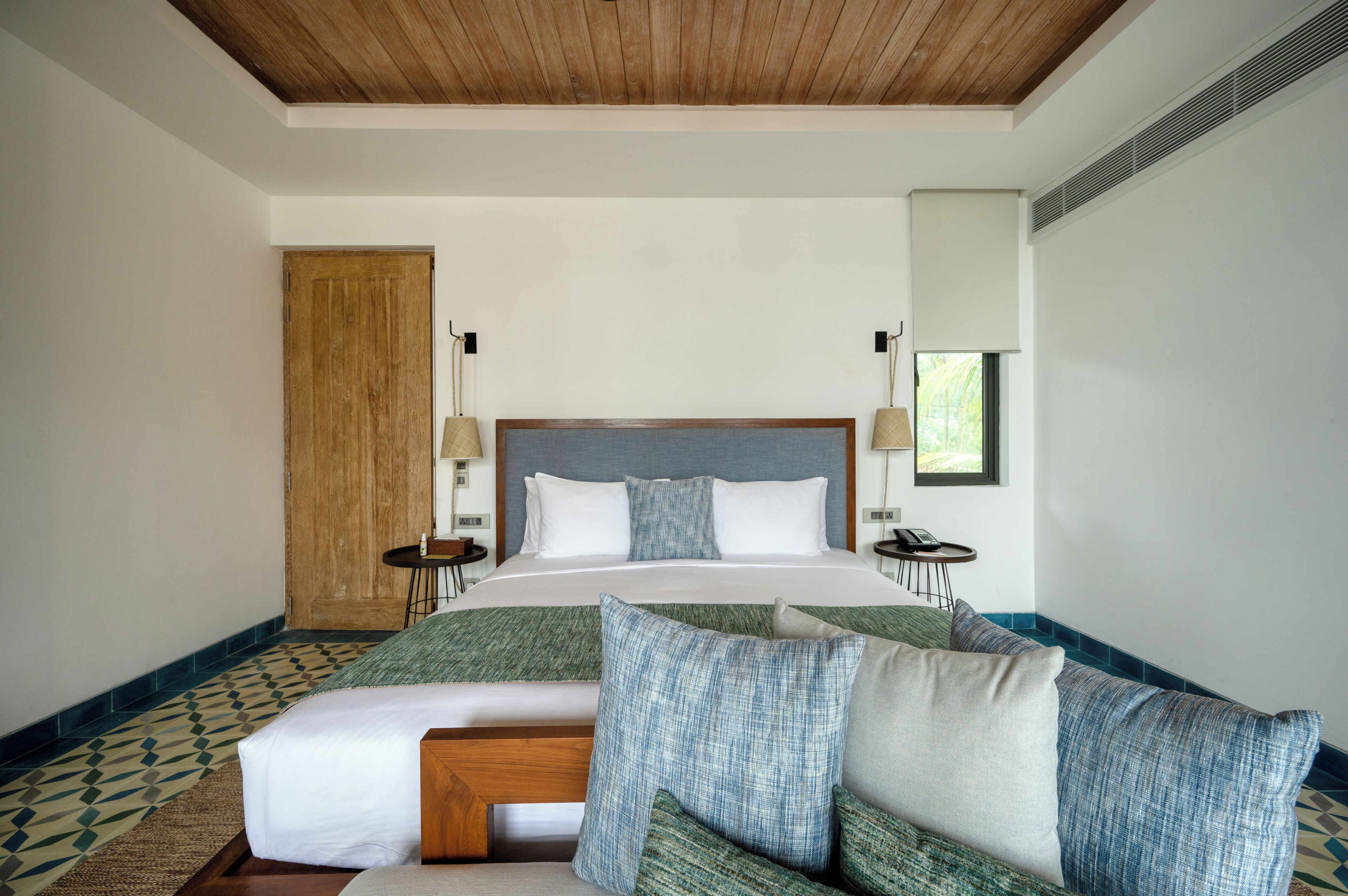 A hotel room with a large bed, wooden ceiling, and a patterned floor.