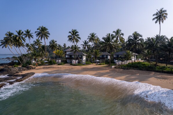 Une propriété située en bord de mer, comprenant plusieurs maisons, des palmiers et une plage de sable.