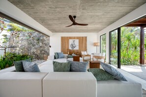 A modern living room with a large sofa, a ceiling fan, and a view of greenery outside. - Ahu Bay (Ahungalla)