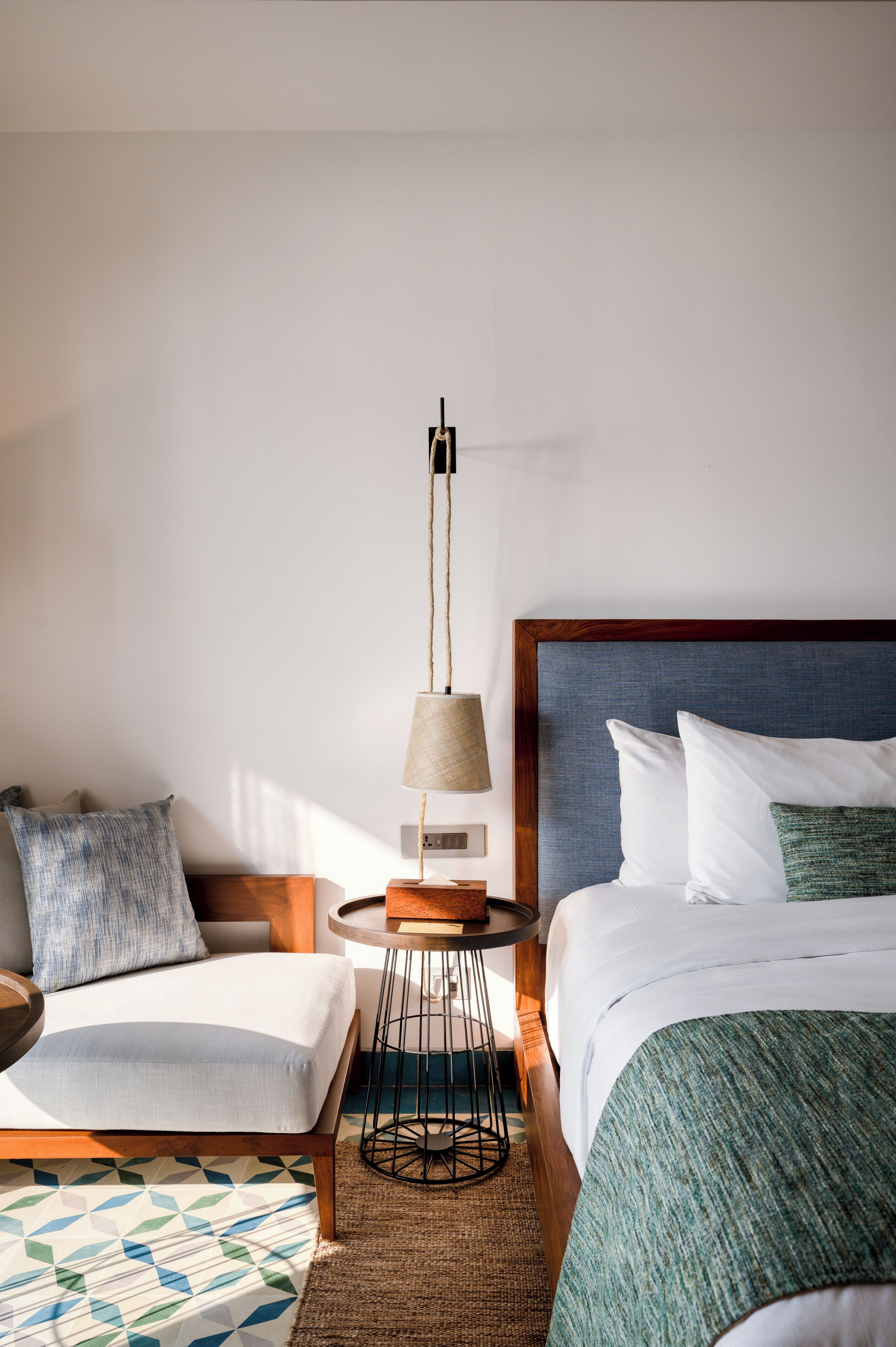 Une chambre d’hôtel avec un lit, un canapé, une petite table ronde avec une lampe et un tapis à motifs.