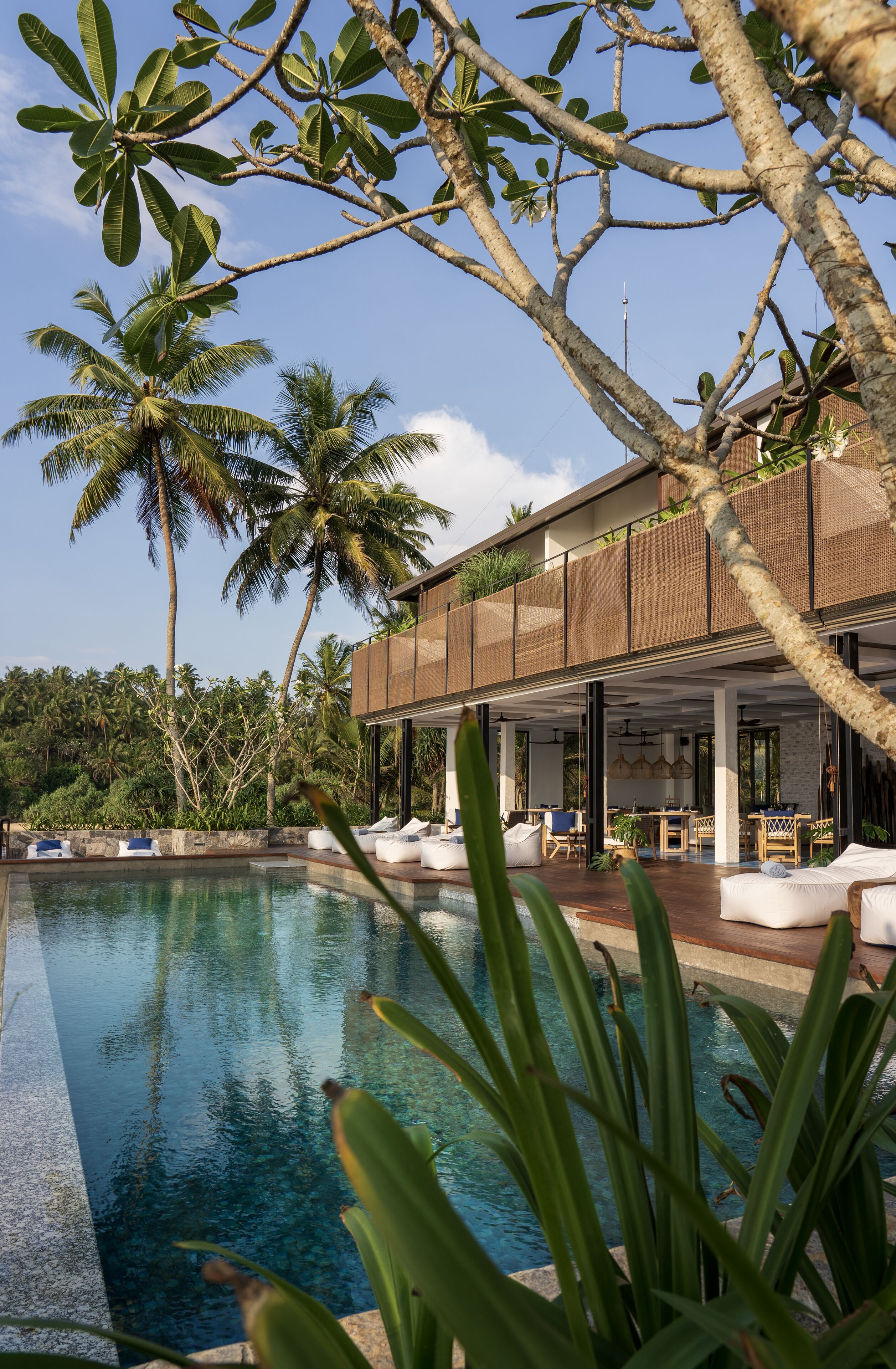 A modern resort with a swimming pool, outdoor seating, and lush tropical vegetation.