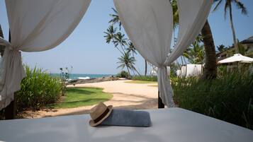 A beach view with a bed, a straw hat, and white curtains.
