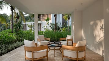 Un espacio al aire libre moderno con cuatro sillas de madera y una mesa redonda, rodeado de abundante vegetación y palmeras.