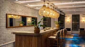 Un área de bar moderna con mostrador de madera, piso con patrón hexagonal y techo de bambú.