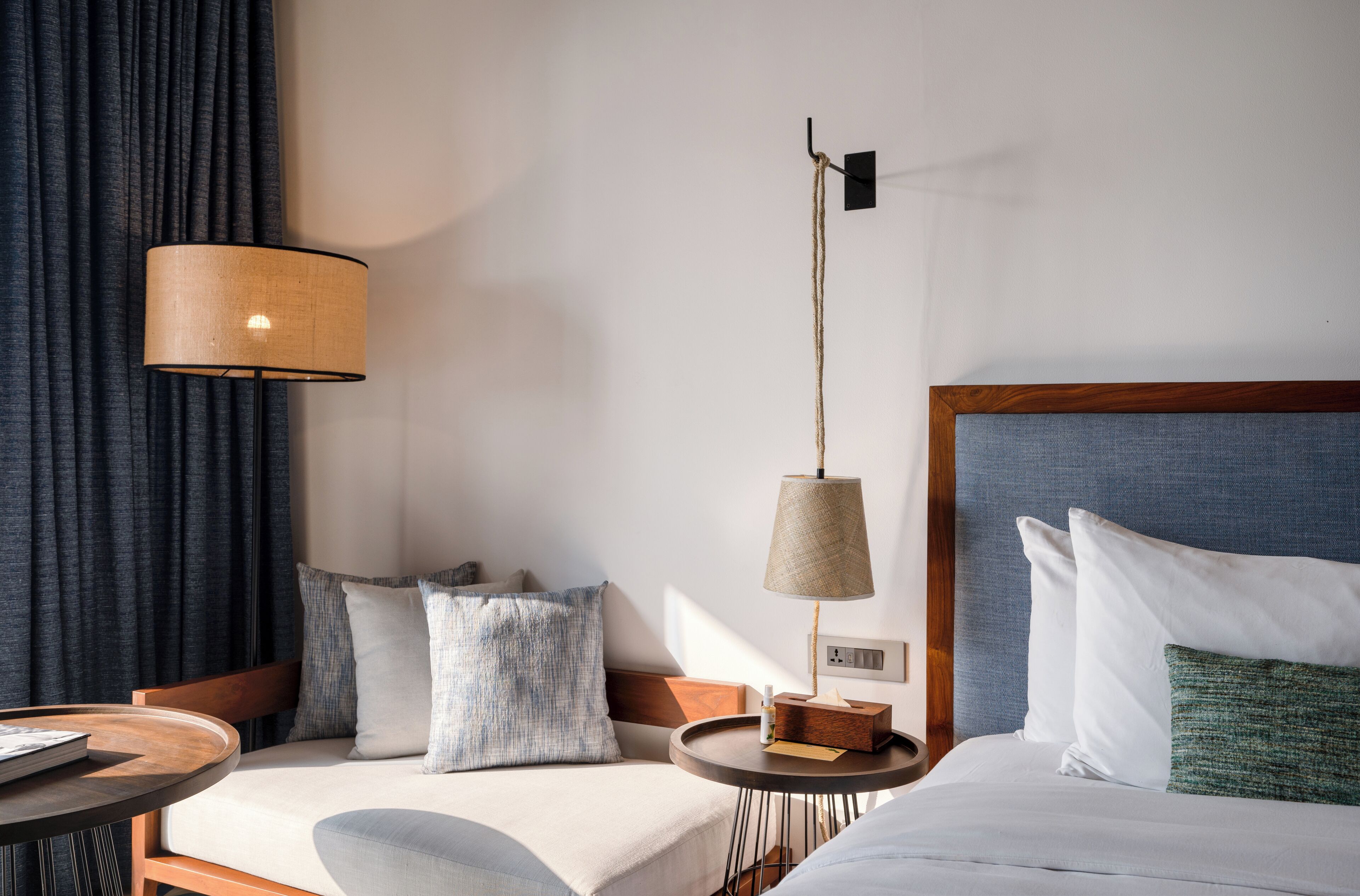 Habitación de hotel con cama, mesita de noche, lámpara y vistas al exterior.