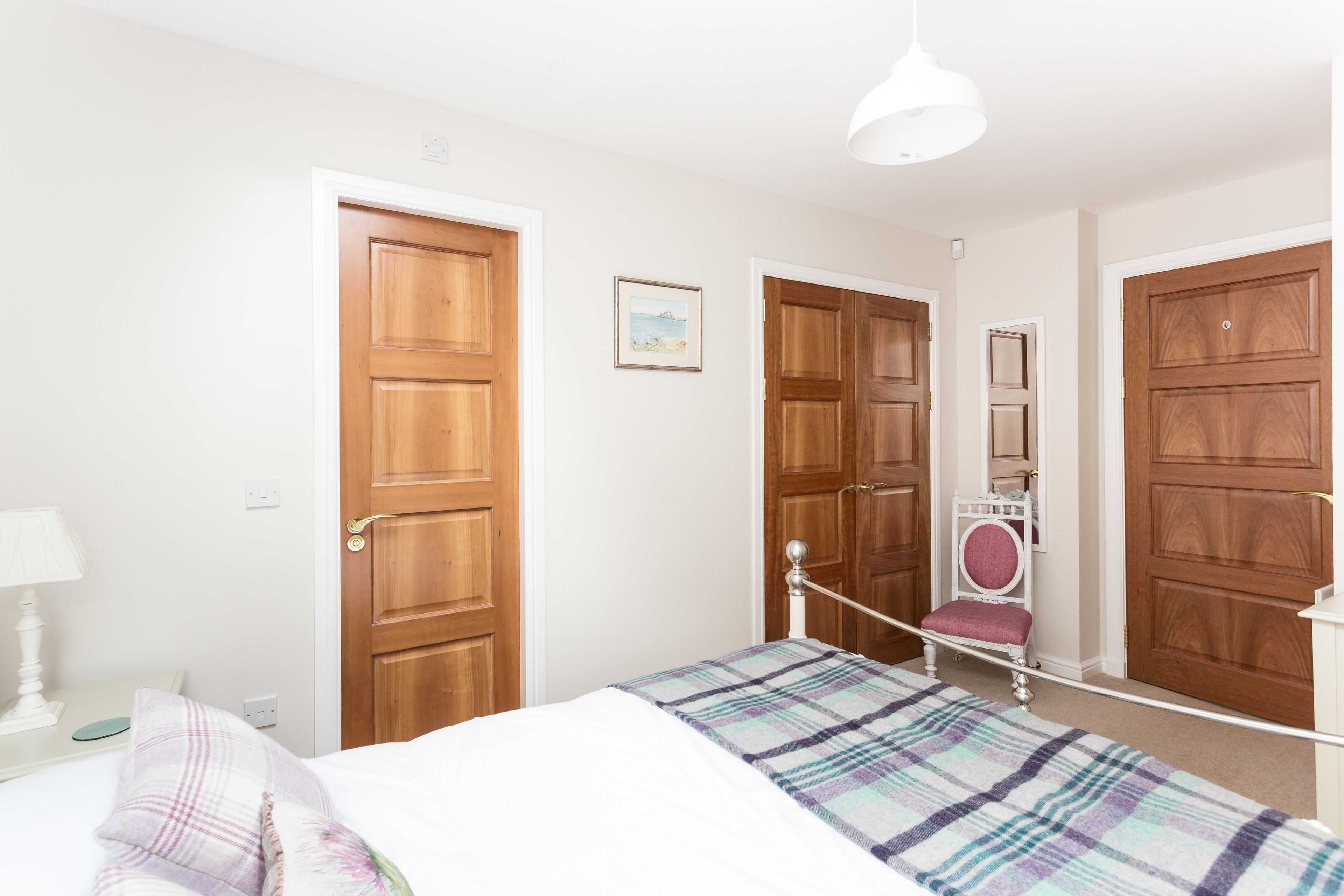 A bedroom with a bed, a nightstand, a lamp, and a wooden wardrobe.