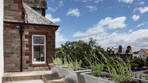 A residential building with a brick facade, a window with a white frame, and a clear sky with clouds. - An Sulaire (North Berwick)