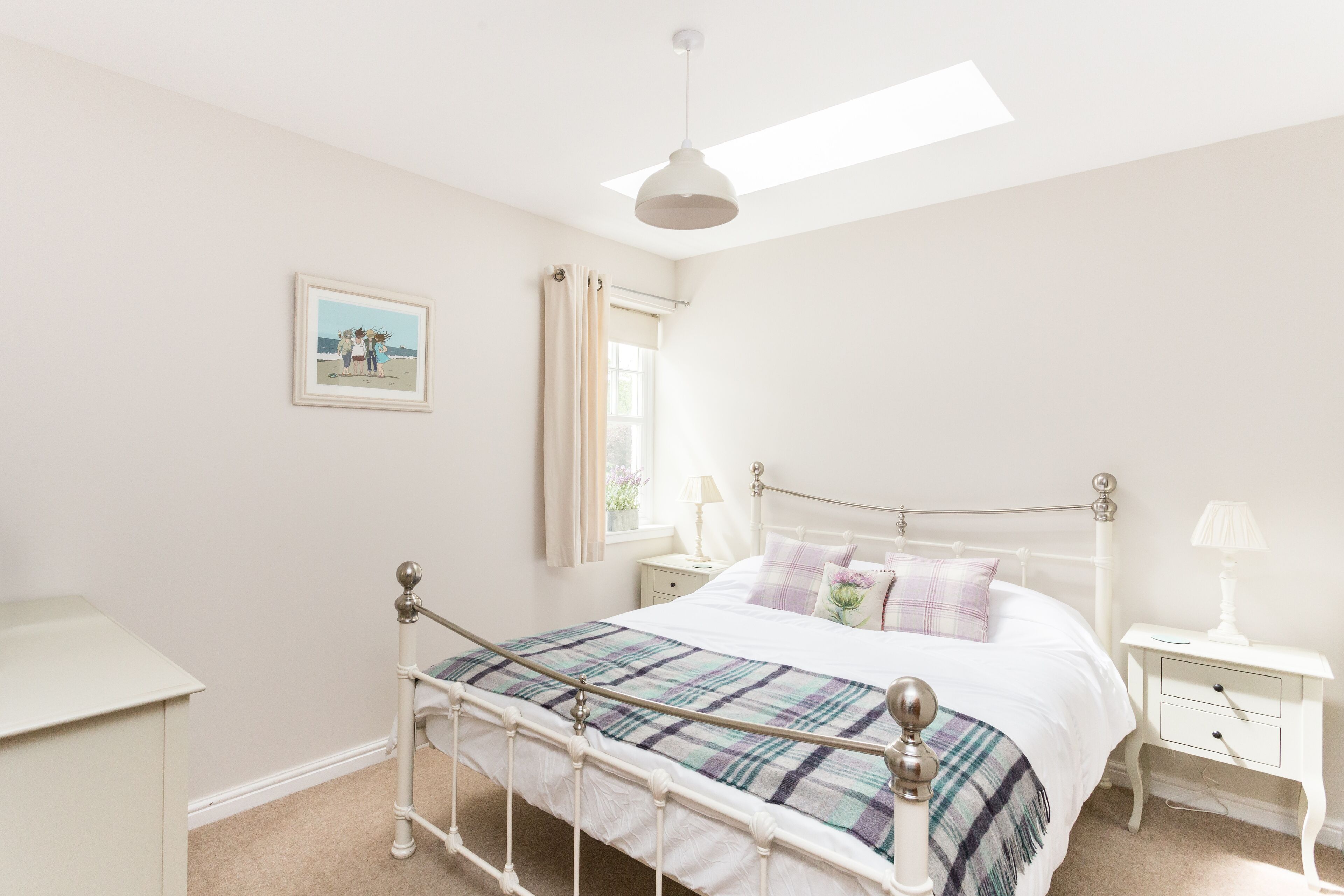 Une chambre à coucher avec un lit, des tables de chevet, une fenêtre avec des rideaux, un ventilateur de plafond et un tableau encadré au mur.