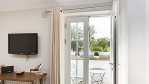 A room with a television mounted on the wall, a wooden table with a bowl and a bird sculpture, and a sliding glass door leading to an outdoor seating area with a table and chairs. - An Sulaire (North Berwick)