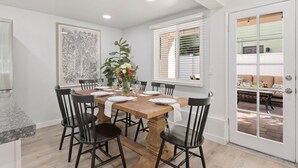 Un comedor con una mesa de madera dispuesta para seis personas, rodeada de sillas negras. En la mesa hay un florero con flores, y en la pared, un cuadro con motivos florales.
