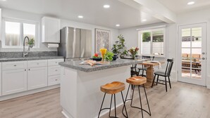 Una cocina moderna con armarios blancos, encimera de granito y una isla central con taburetes.