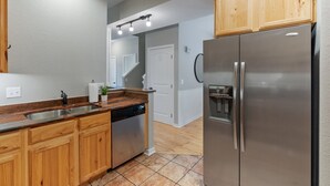 A modern kitchen with wooden cabinets, a stainless steel refrigerator, and a dishwasher. - Red Barn Roost • Cozy Stay Near Downtown (Loveland)