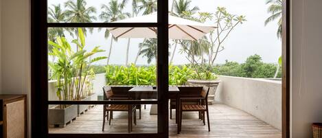 A balcony with a wooden table and chairs, potted plants, and a large umbrella.