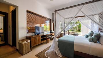 A bedroom with a bed, TV, wooden desk, and a view of greenery outside.
