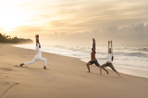 Three people practicing yoga on a beach with the ocean and a sunset in the background.