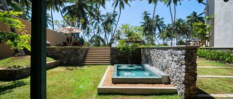 Un espacio al aire libre techado con un muro de piedra, una pequeña piscina y una escalera que sube a un nivel superior.
