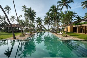 Una piscina con palmeras y sillones de descanso.