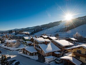 A snow-covered village with traditional chalet-style buildings, a clear sky, and a sunlit landscape. - Vierbettzimmer mit Bad, WC - HP - Golf- und Skipension Krug (Haus)