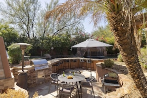 Landscaped outdoor lounge area shaded dining, evening lights, and a BBQ/grill.