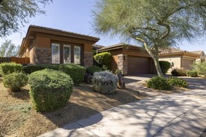 A residential house with a stone facade, a garage, and well-maintained landscaping including bushes and a tree.