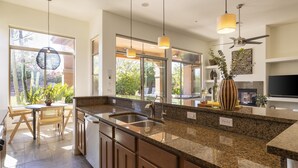 Cozinha moderna com bancadas de granito, eletrodomésticos de aço inoxidável e iluminação pendente.
