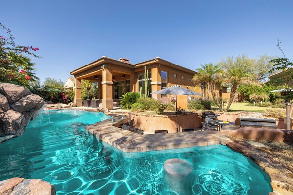 Un espace piscine avec une maison, un coin salon extérieur et un jardin bien entretenu.