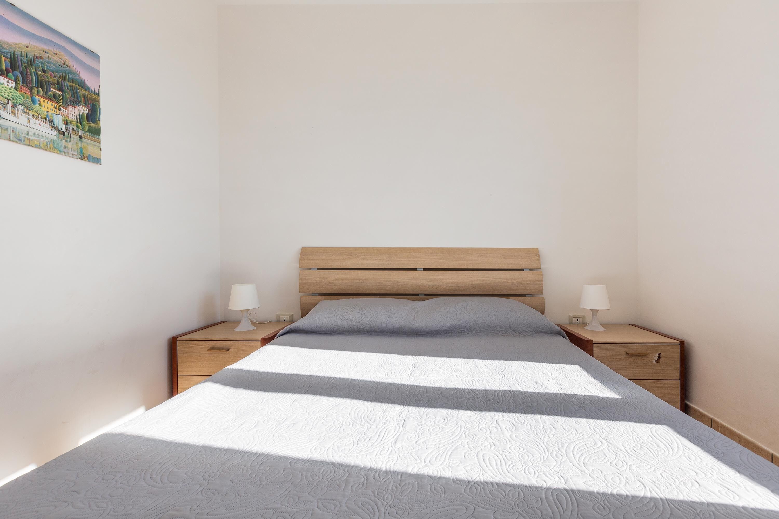 A bedroom with a wooden bed, two bedside tables with lamps, and a painting on the wall.
