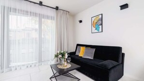 Una sala de estar moderna con un sofá negro, una mesa de centro y un ventanal con cortinas de gasa.