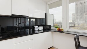 Una cocina moderna con armarios blancos, encimera negra, microondas, hervidor y frutero.