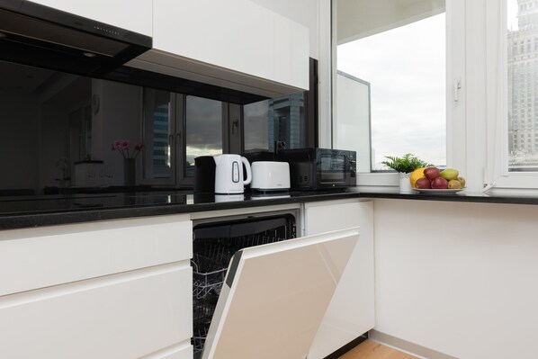 Una cocina moderna con armarios blancos, encimera negra, cafetera, microondas y frutero.