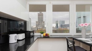 Una cocina moderna con encimera negra, armarios blancos y vistas a un paisaje urbano a través de grandes ventanales.