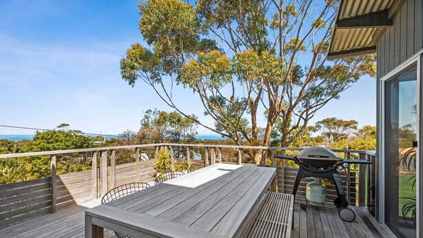 A wooden deck with a table and chairs, a barbecue grill, and a view of the ocean. - Beach Comber (Anglesea)