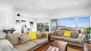 A modern living room with two sofas, a coffee table, and a kitchen in the background. - Beach Comber (Anglesea)