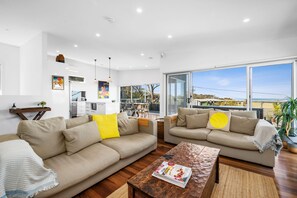 A modern living room with two sofas, a coffee table, and a kitchen in the background. - Beach Comber (Anglesea)