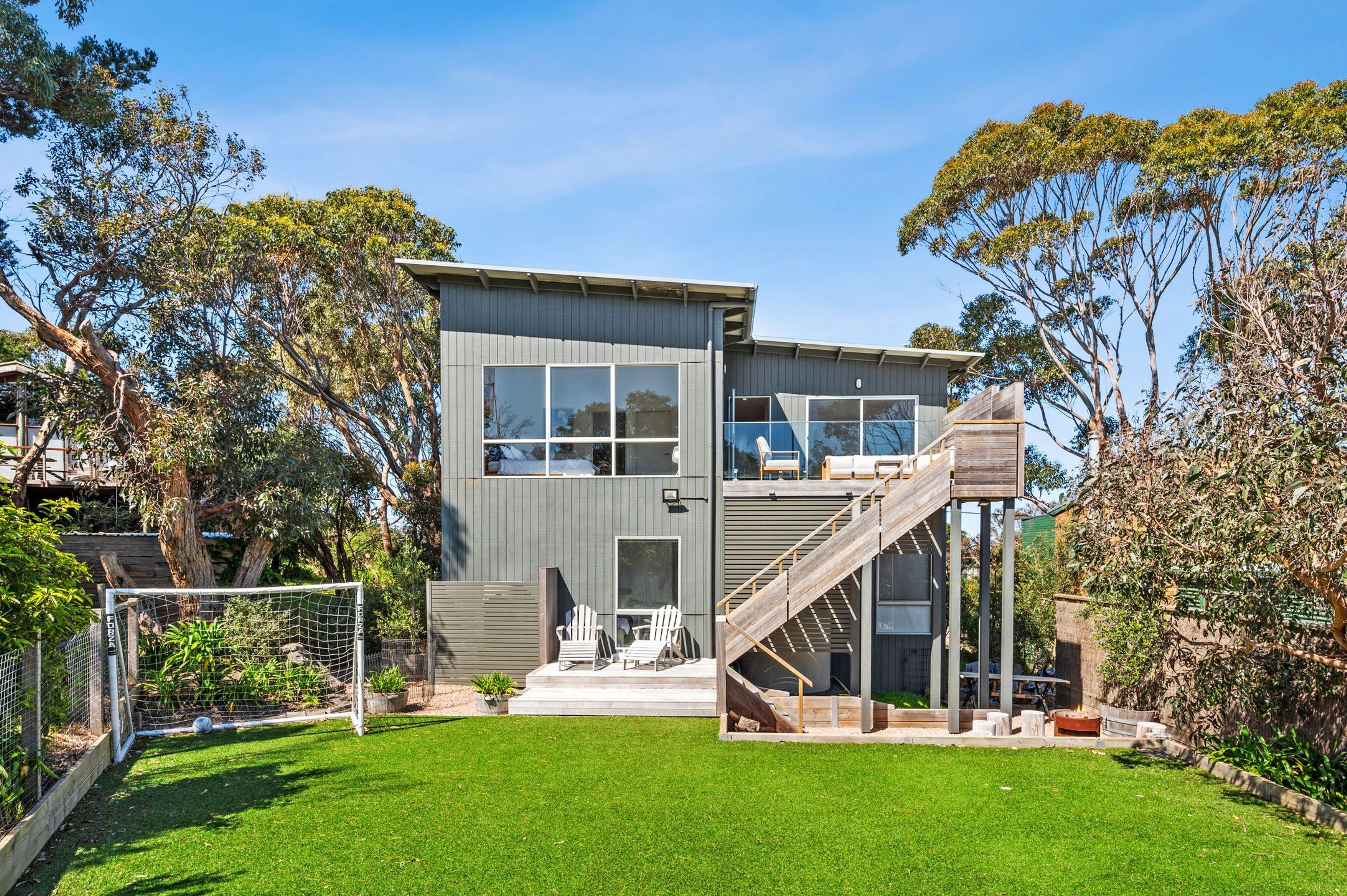 A modern two-story house with a large deck and a staircase leading to an upper level.