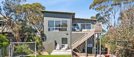 A modern two-story house with a large deck and a staircase leading to an upper level.