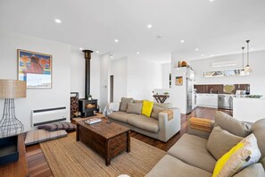 A modern living room with a fireplace, a sofa, a coffee table, and a kitchen in the background. - Beach Comber (Anglesea)