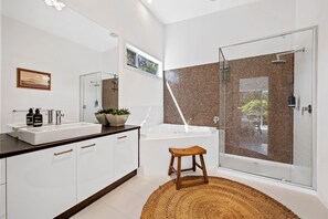 A modern bathroom with a white vanity, a bathtub, and a glass-enclosed shower area. - Beach Comber (Anglesea)