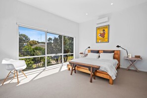 A bedroom with a large window, a bed, a bedside table, a lamp, and a poster on the wall. - Beach Comber (Anglesea)