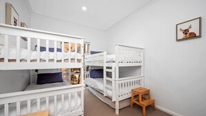 A room with bunk beds, a small wooden stool, and a framed picture on the wall. - Beach Comber (Anglesea)